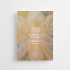 Postkarte "Bloom in the Dark" im DIN-A6-Format von Anna Cosma mit einem zarten, floralen Hintergrund in warmen Pastell- und Erdtönen sowie dem weißen Text „Bloom in the dark. Bloom in the light. Bloom anyway.“