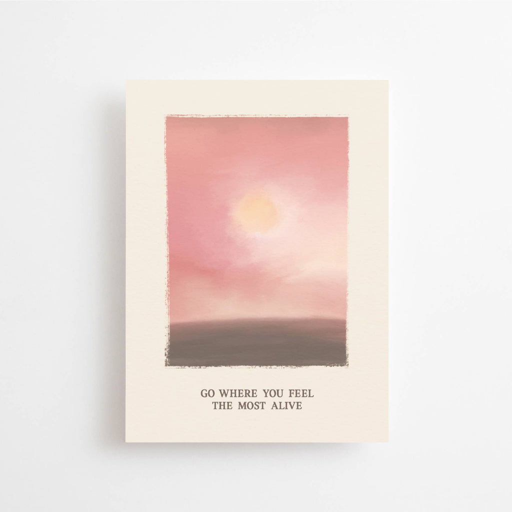 Postkarte „Go where you feel the Most Alive“ im DIN-A6-Format mit einer stimmungsvollen Illustration in Rosé-Tönen, einer sanften Sonne und dem Schriftzug vor hellem Hintergrund.