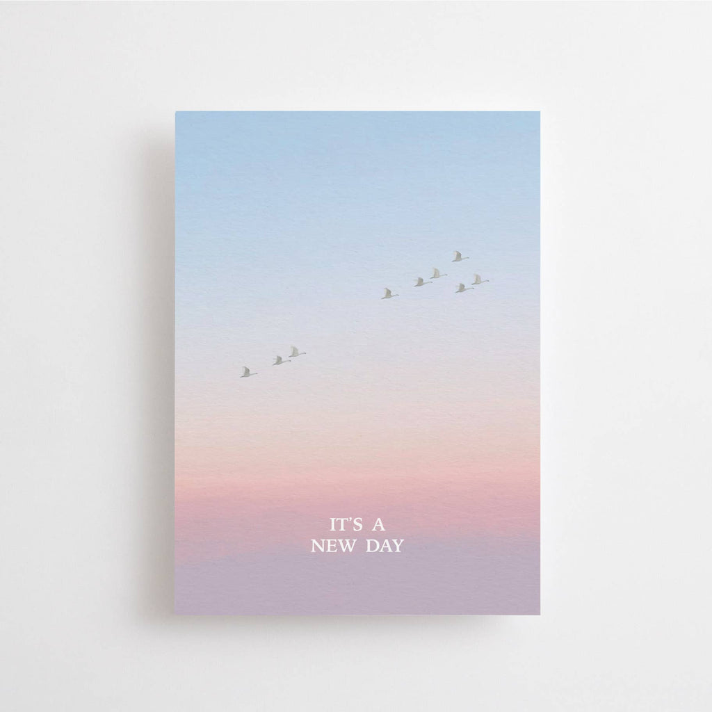 Postkarte „It's a New Day“ im DIN-A6-Format mit einem stimmungsvollen Farbverlauf, fliegenden Vögeln und dem Schriftzug vor einer natürlichen Landschaft.