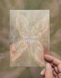 Postkarte "You are Divine" im DIN-A6-Format von Anna Cosma mit einem abstrakten, blütenartigen Motiv in sanften Naturtönen und dem weißen Text „YOU ARE DIVINE“.
