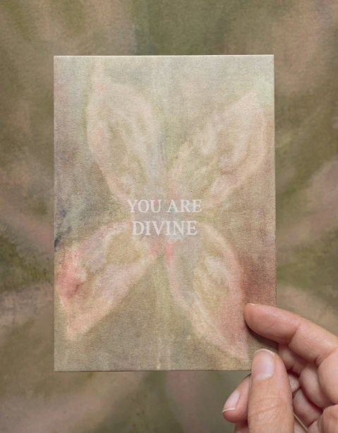 Postkarte "You are Divine" im DIN-A6-Format von Anna Cosma mit einem abstrakten, blütenartigen Motiv in sanften Naturtönen und dem weißen Text „YOU ARE DIVINE“.
