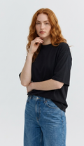 Weibliches Model mit rötlichen Haaren trägt ein schwarzes Black Lena Tee von Thinking Mu mit Rundhalsausschnitt zu blauen Jeans.
