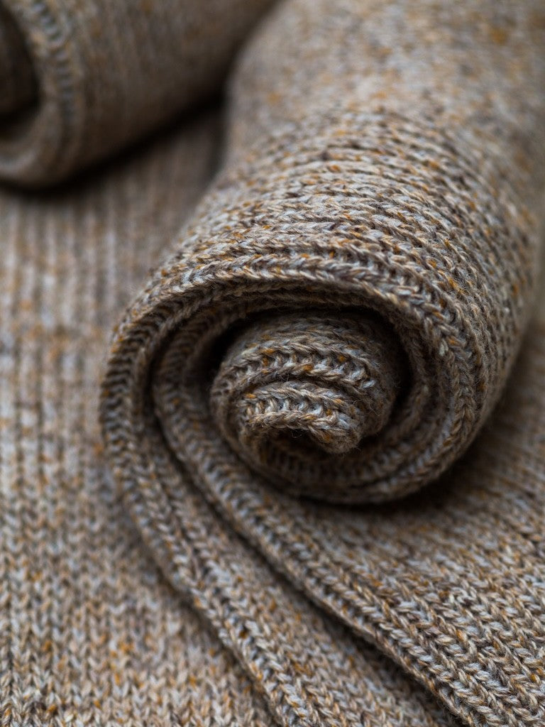 Zusammengelegte melierte Stricksocken aus Merinowolle und Seide im Naturton mit schwarzer Ferdinand-Banderole vor hellem Hintergrund.