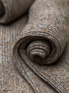Zusammengelegte melierte Stricksocken aus Merinowolle und Seide im Naturton mit schwarzer Ferdinand-Banderole vor hellem Hintergrund.