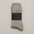 Zusammengelegte melierte Stricksocken aus Merinowolle und Seide im Naturton mit schwarzer Ferdinand-Banderole vor hellem Hintergrund.