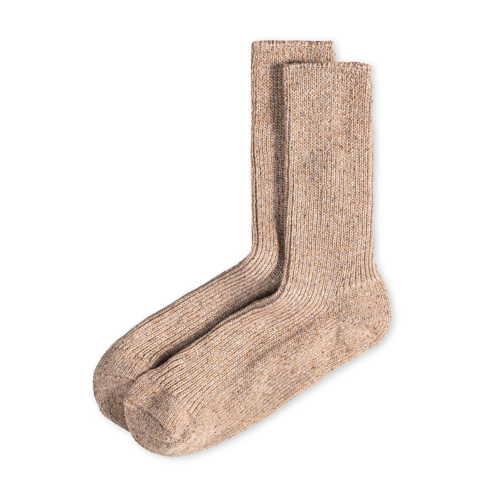 Zusammengelegte melierte Stricksocken aus Merinowolle und Seide im Naturton mit schwarzer Ferdinand-Banderole vor hellem Hintergrund. koblenz
