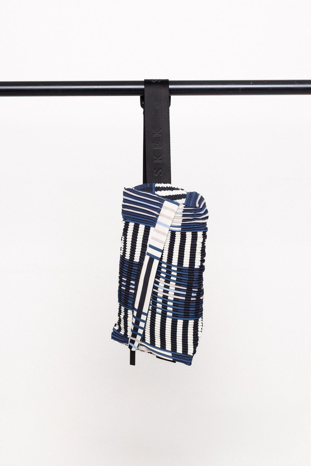Detailansicht der ADOR BAG mit Fokus auf die diagonalen Plissees und den schwarzen Nylonriemen, hängend an einer Stange.