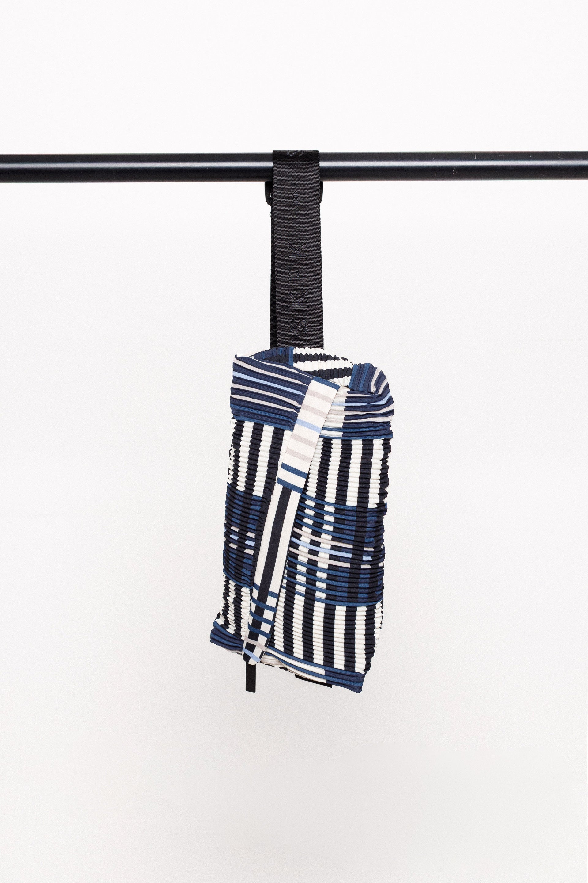 Detailansicht der ADOR BAG mit Fokus auf die diagonalen Plissees und den schwarzen Nylonriemen, hängend an einer Stange.