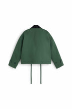 Grüne Jacke "Norma" von Thinking Mu mit dunklem Cord-Kragen, Knöpfen und herabhängenden Bändern am Saum vor hellem Hintergrund.