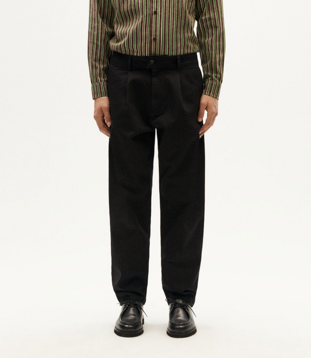 Klassische schwarze Hose "Wotan" von Thinking Mu aus Bio-Baumwolle in gerader Passform vor hellem Hintergrund.