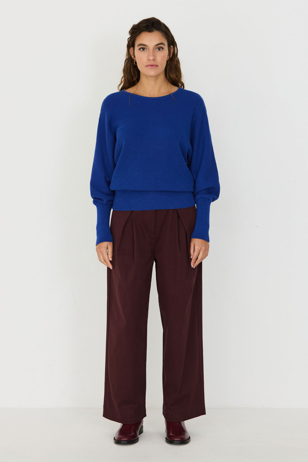 Person von vorne in einem blauen Strickpullover "Ibar" mit runden Halsausschnitt und Dolman-Ärmeln vor hellem Hintergrund.