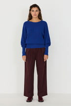 Person von vorne in einem blauen Strickpullover "Ibar" mit runden Halsausschnitt und Dolman-Ärmeln vor hellem Hintergrund.