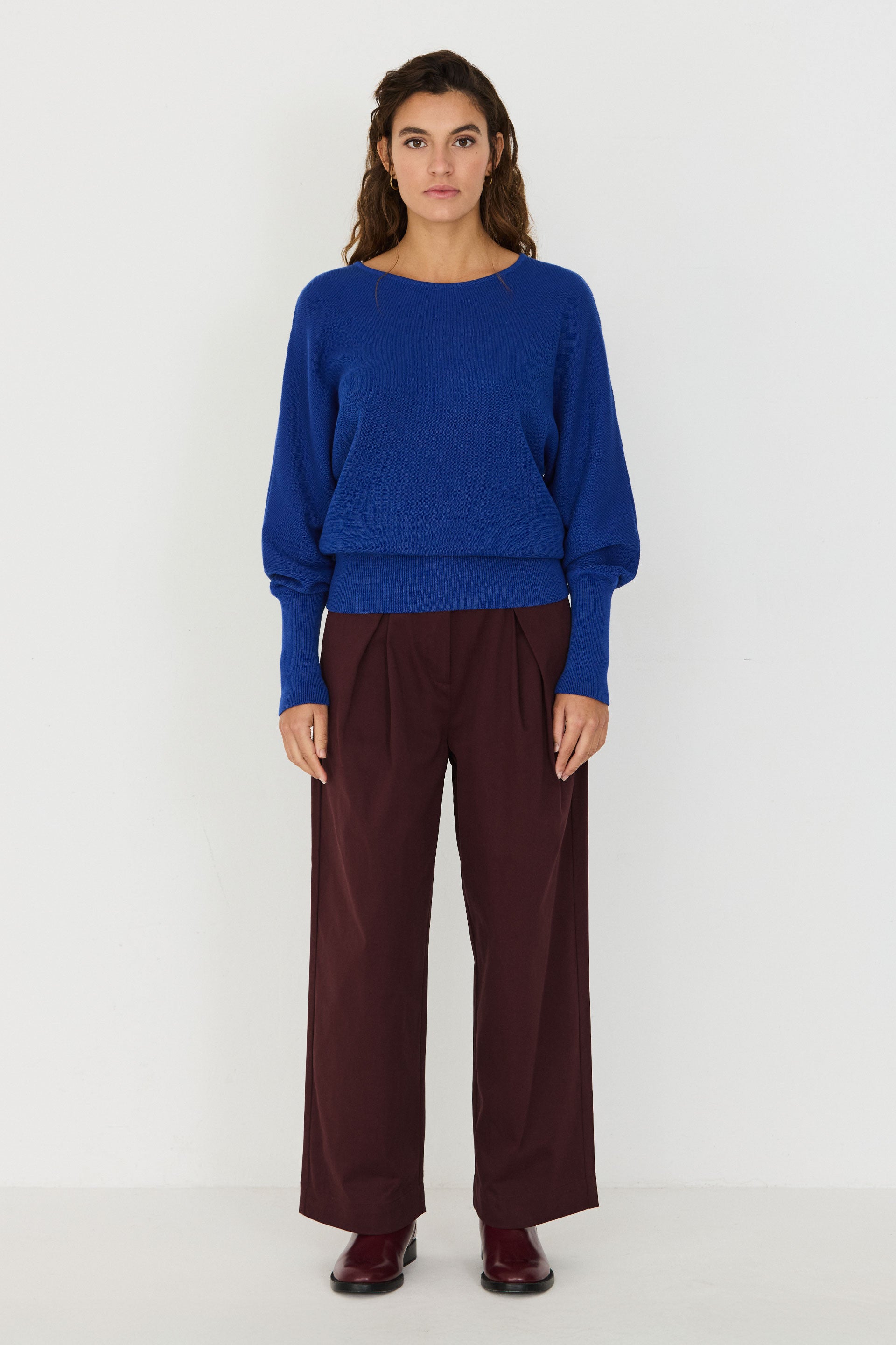 Person von vorne in einem blauen Strickpullover "Ibar" mit runden Halsausschnitt und Dolman-Ärmeln vor hellem Hintergrund.