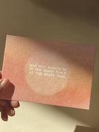 Postkarte „Right Place Right Time“ im DIN-A6-Format mit einem warmen rosafarbenen Farbverlauf, einem zentralen Lichtkreis und dem englischen Schriftzug vor hellem Hintergrund.