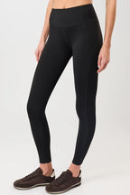 Person von vorne in einer schwarzen High-Rise-Leggings "Limitless" mit dynamischen Teilungsnähten und dunklen Sneakern vor hellem Hintergrund.