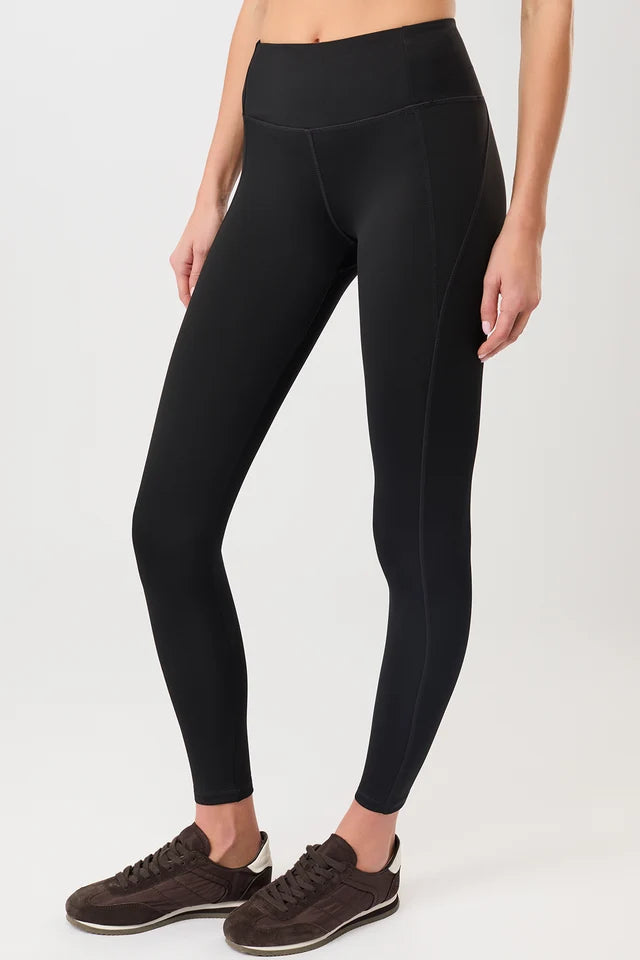 Person von vorne in einer schwarzen High-Rise-Leggings "Limitless" mit dynamischen Teilungsnähten und dunklen Sneakern vor hellem Hintergrund.