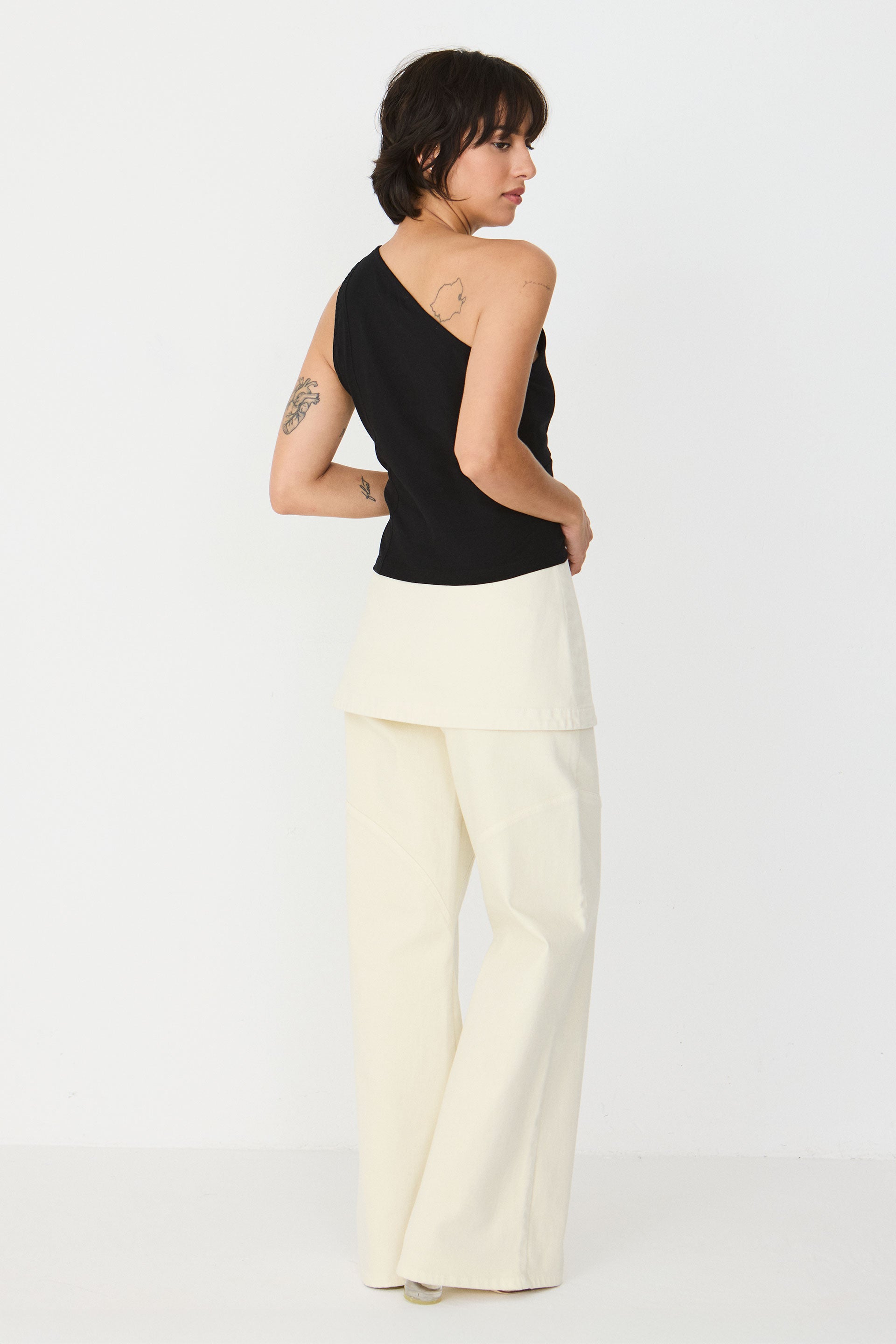 Model trägt das schwarze Kris-Gots T-Shirt der Marke SKFK im One-Shoulder-Stil mit Keyhole-Ausschnitt zu einem hellen Rock.