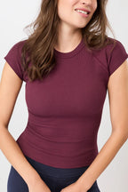 Person von vorne in einem dunkelroten, gerippten Slim-Fit-T-Shirt mit kurzen Ärmeln und Raglanschnitt vor hellem Hintergrund.