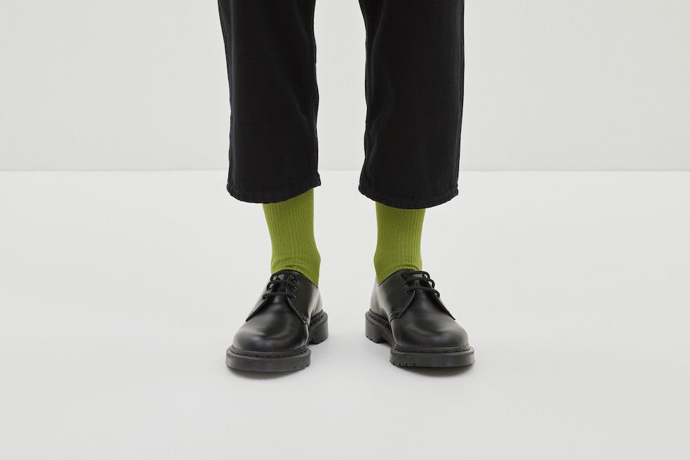 Grüne Socken Luji im Rippstrick-Design mit nahtloser Fußspitze, abgebildet als flach liegendes Produkt und getragen mit schwarzen Schuhen.
