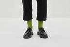 Grüne Socken Luji im Rippstrick-Design mit nahtloser Fußspitze, abgebildet als flach liegendes Produkt und getragen mit schwarzen Schuhen.