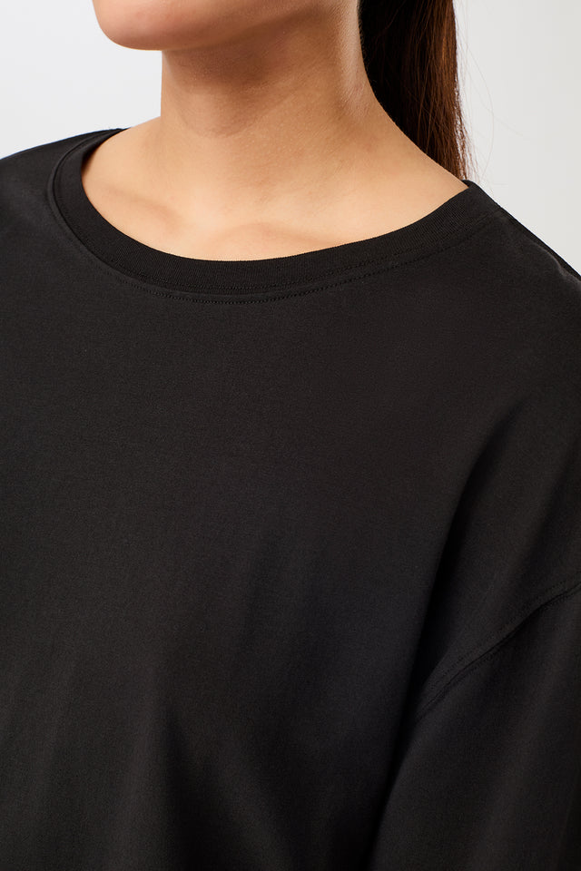 Person von vorne in einem schwarzen, oversized Langarmshirt "Wide" mit rundem Ausschnitt vor hellem Hintergrund.