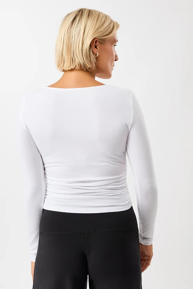 Blonde Frau von vorne in einem weißen Langarmshirt "Side Ruffled" mit Rundhalsausschnitt und seitlichen Raffungen vor hellem Hintergrund.