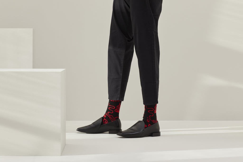 Ein Paar schwarze Socken mit rotem Bund, roter Ferse und Zehenpartie sowie grafischen, roten Figuren- und Tiermotiven auf hellem Hintergrund. koblenz baumwolle