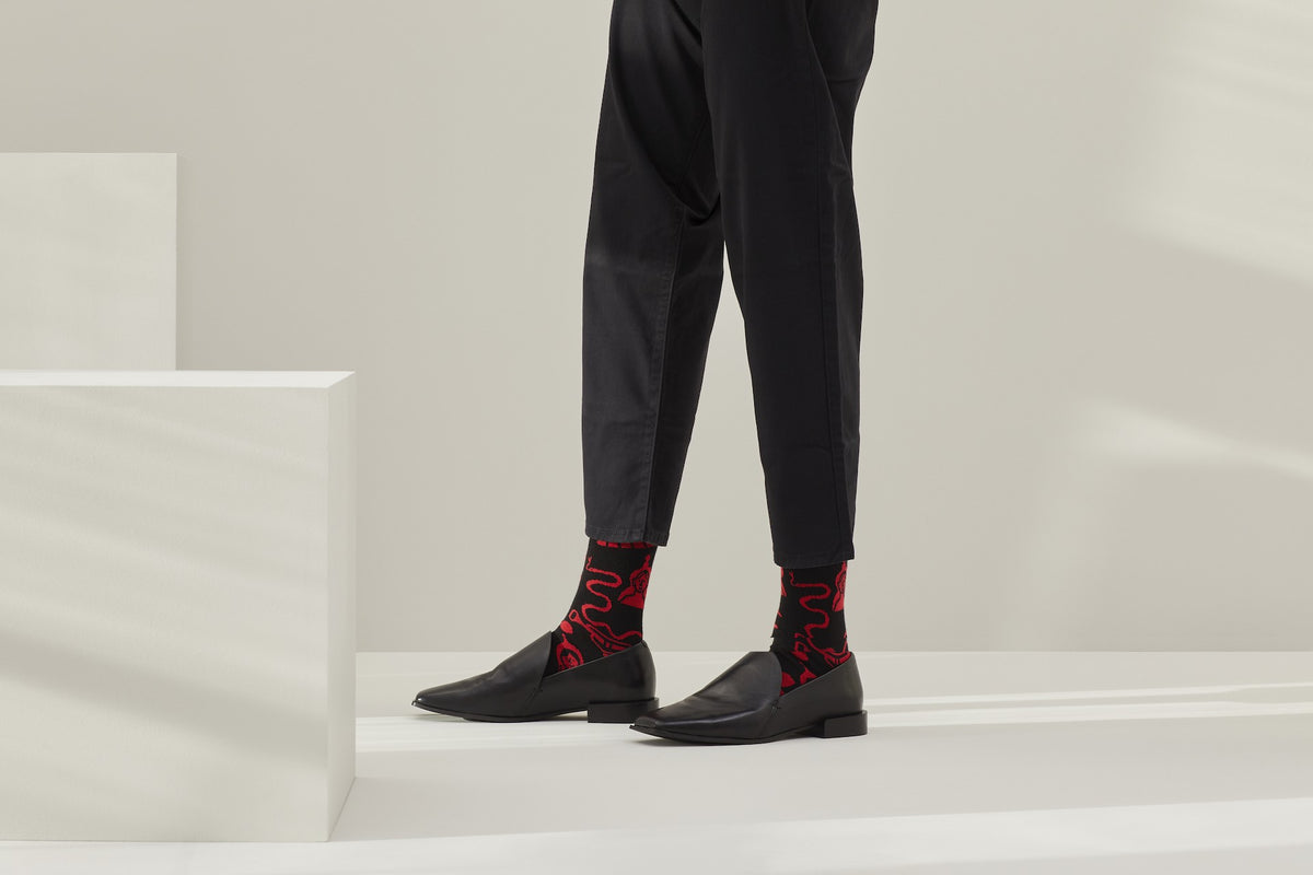 Ein Paar schwarze Socken mit rotem Bund, roter Ferse und Zehenpartie sowie grafischen, roten Figuren- und Tiermotiven auf hellem Hintergrund. koblenz baumwolle