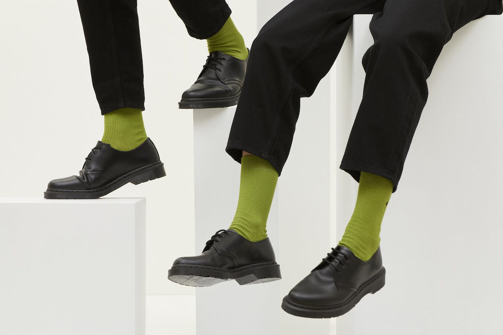 Grüne Socken Luji im Rippstrick-Design mit nahtloser Fußspitze, abgebildet als flach liegendes Produkt und getragen mit schwarzen Schuhen.