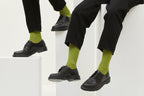 Grüne Socken Luji im Rippstrick-Design mit nahtloser Fußspitze, abgebildet als flach liegendes Produkt und getragen mit schwarzen Schuhen.