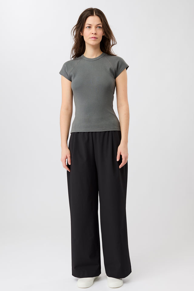 Person von vorne in einem dunkelgrauen, gerippten Slim-Fit-T-Shirt mit kurzen Ärmeln und Raglanschnitt vor hellem Hintergrund.