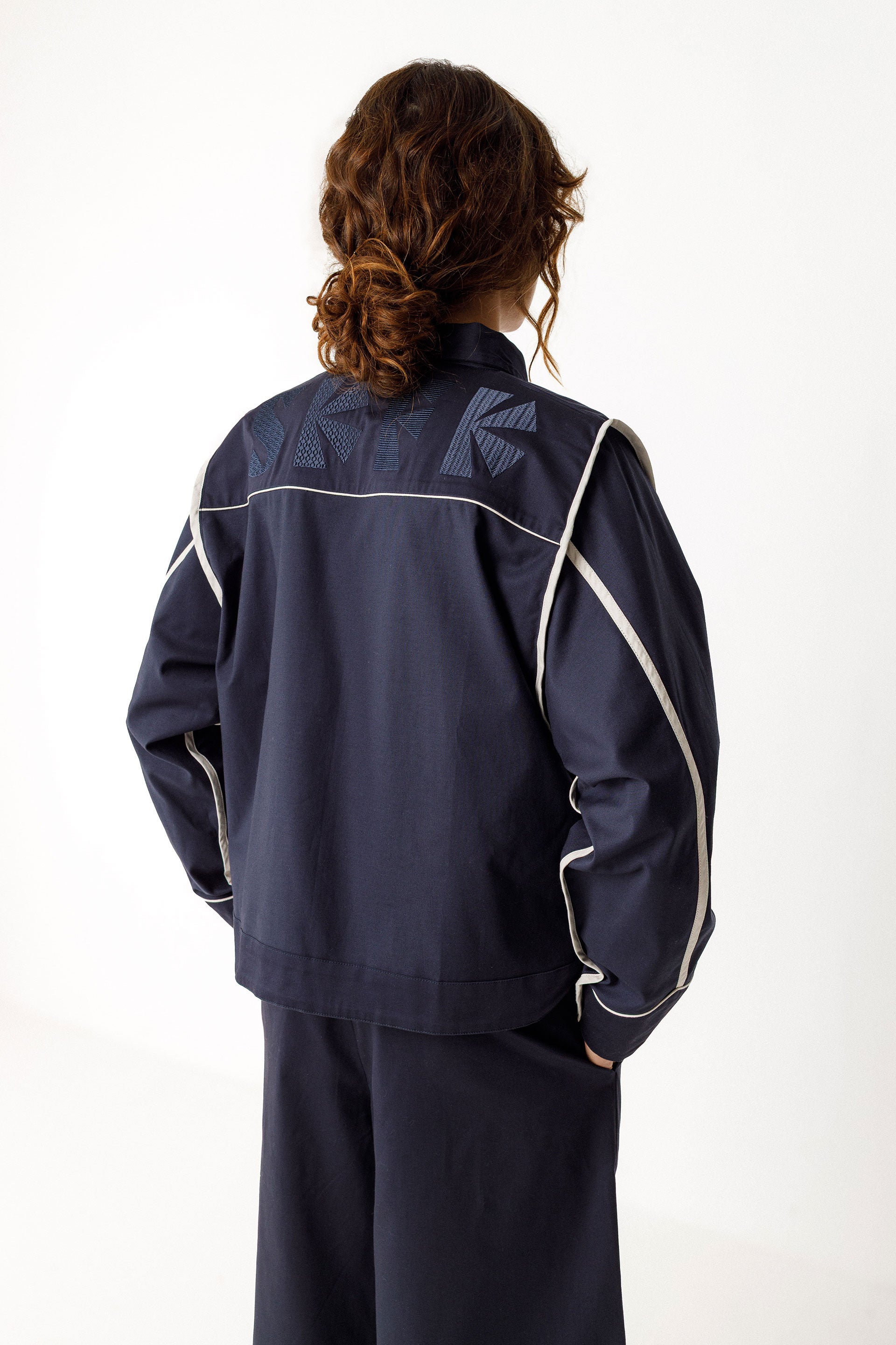 Rückansicht der HALTSU Wendejacke mit hellen Kontrastpaspeln und eingearbeitetem Logo.