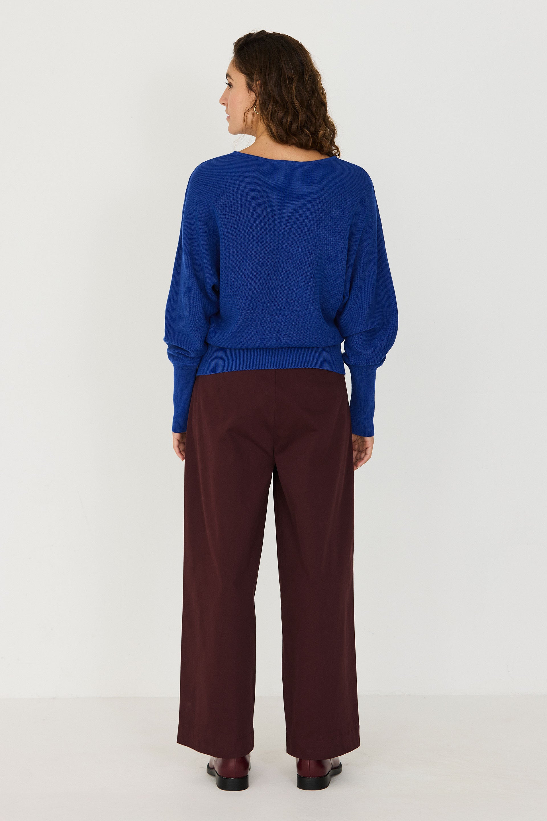 Person von vorne in einem blauen Strickpullover "Ibar" mit runden Halsausschnitt und Dolman-Ärmeln vor hellem Hintergrund.