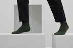 Ein Paar gestrickte Socken aus Wolle in meliertem Waldgrün vor weißem Hintergrund.