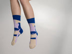 Ein Paar blaue Socken mit beigen und violetten, abstrakten Farb- und Blockmustern sowie beiger Fersen- und Zehenpartie vor hellem Hintergrund. koblenz baumwolle