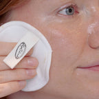 Sieben weiße, runde Make-up-Pads auf einem hellen Fliesenboden neben einem geöffneten Netzbeutel.